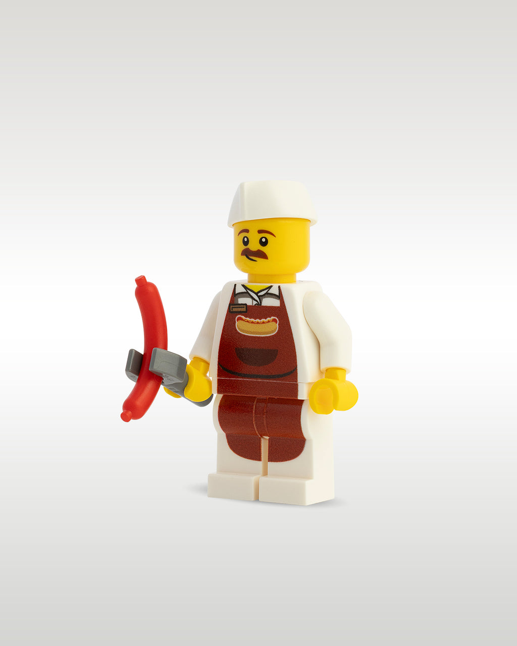 view of the Trader Bricks custom printed food vendor minifig proudly holding a miniature toy hot dog sausage