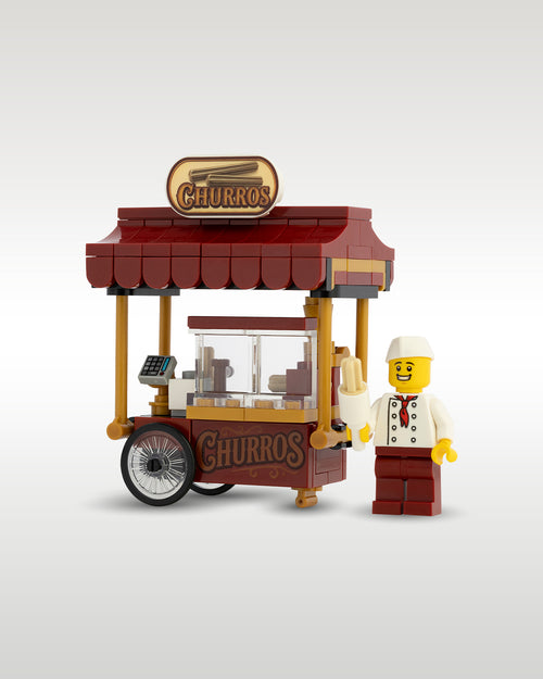 Custom brick-built Churro food cart MOC set by Trader Bricks, featuring a dark red awning, custom printed Churros signs, a cash register, and a street food vendor minifigure