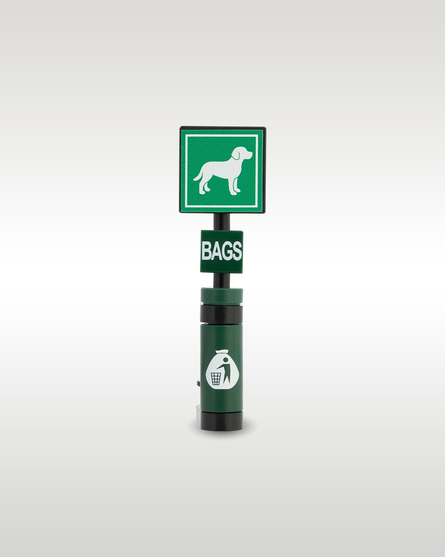 Custom brick-built pet clean up station model by Trader Bricks, featuring a green square sign with a custom printed white dog graphic, a 'BAGS' dispenser tile, and a dark green trash bin